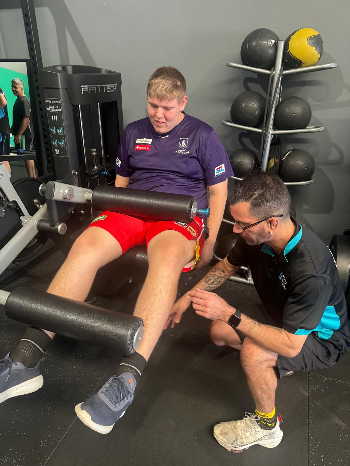 A support worker coaching a teenager through a gym session