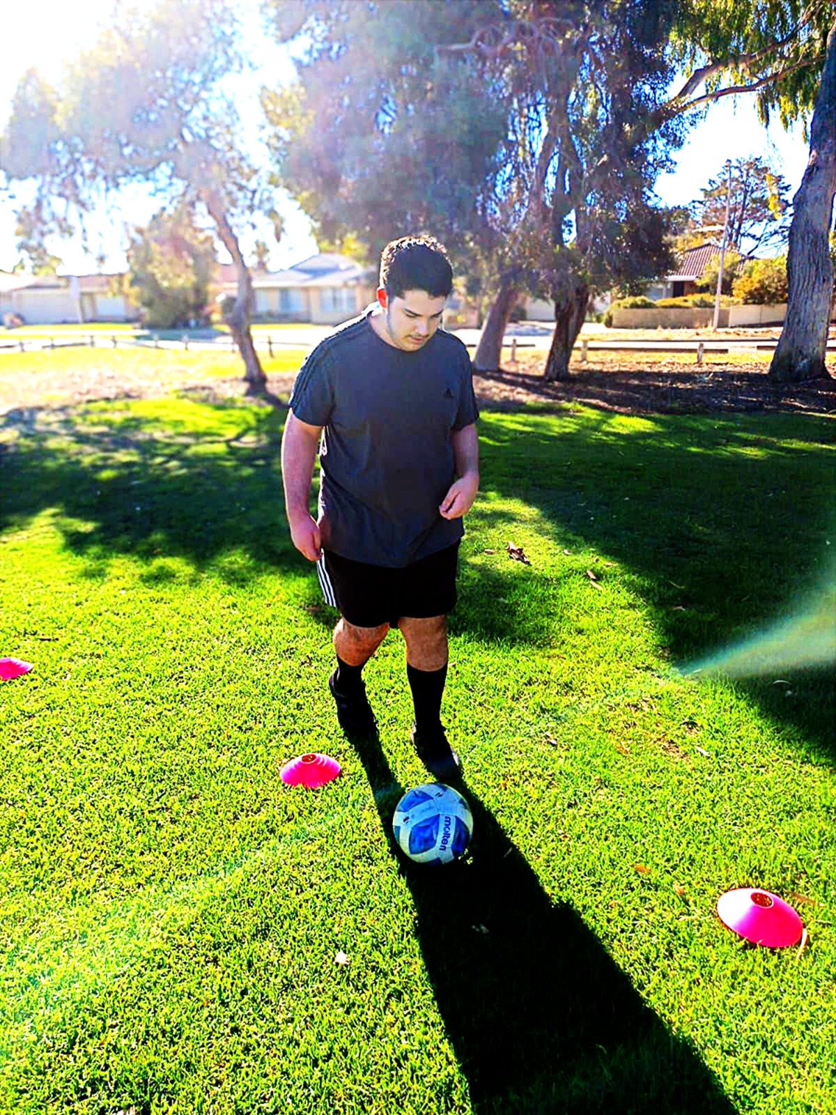 A teenager dribbling a soccer ball through cones in a park